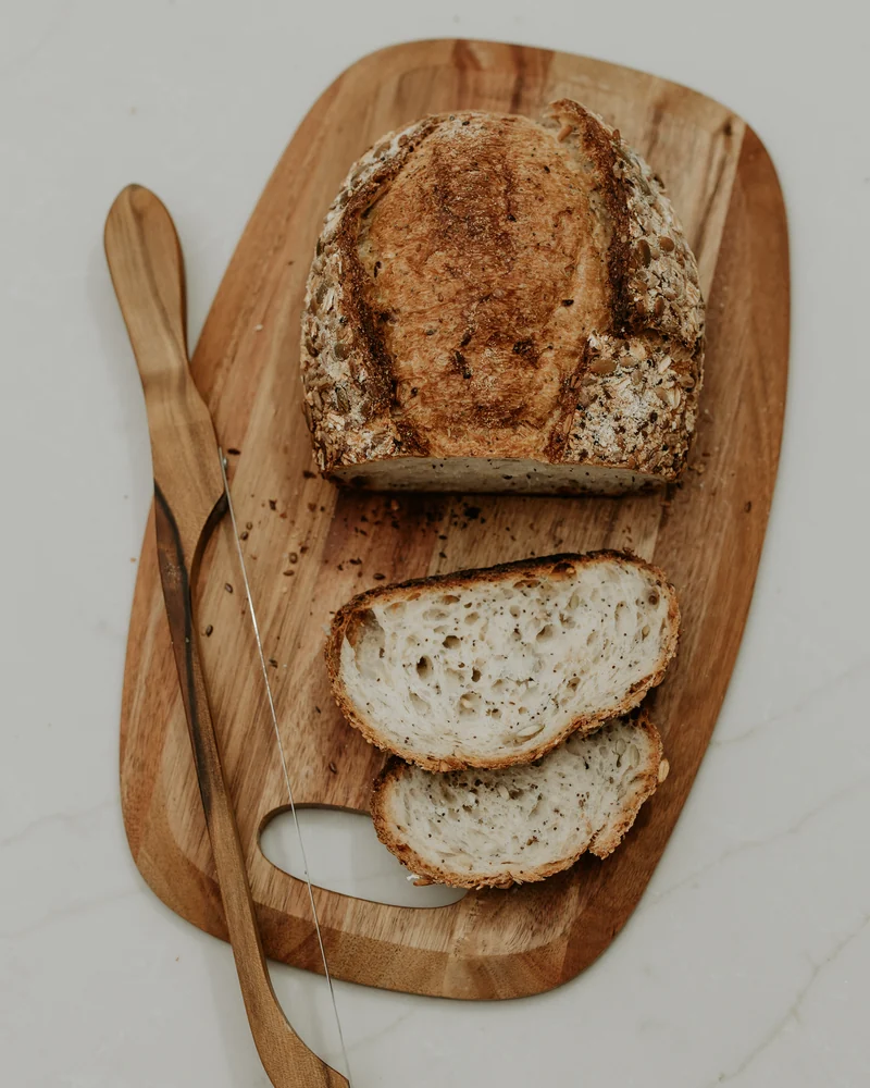 A loaf of seeded sourdough with two slices cut, on a wooden board