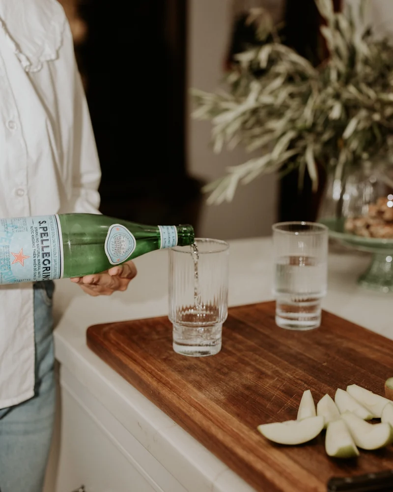 Sparkling water being poured into a glass beside sliced pears on a wooden board