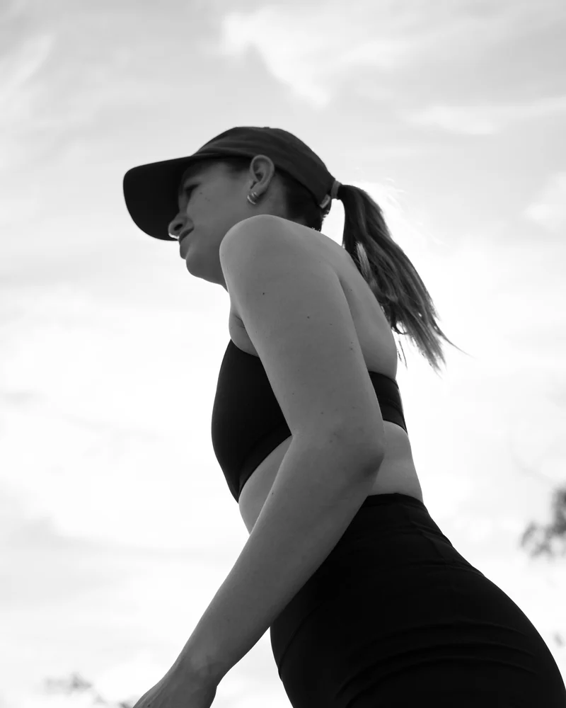 Laura outdoors in a cap and activewear, photographed from below against the sky