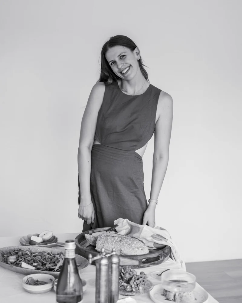 Laura smiling behind a table set with salads, fresh bread and fruit